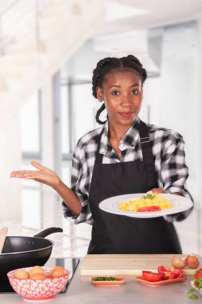 Professional looking afro american woman with an apron offering a plate of delicious scrambled eggs to the camera: Selective focus. Cooking concept.